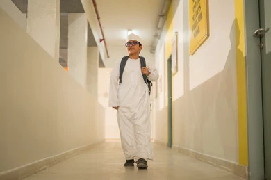 الجد والاجتهاد للوصول إلى النجاح والتفوق، موسم العودة إلى المدارس، طالب عربي خليجي عماني يرتدي الدشداشة و الكمة يحمل حقيبة الظهر المدرسية يمشي فى بهو المدرسة،إيماءات السعادة والفرح