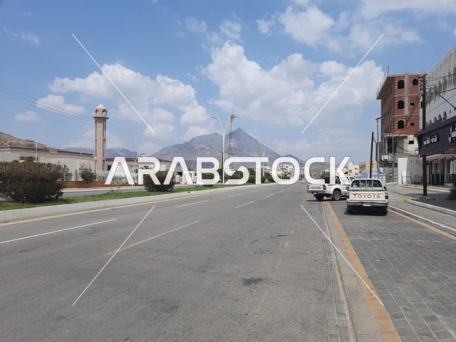 الطرقات الاسفلتية المعبدة في أماكن القمم والمرتفعات الجبلية في وقت النهار، طريق معبد في منطقة الباحة، النباتات الخضراء البرية على حافتي الشارع، أعمدة الإنارة الطرقية، حركة مرور السيارات في الشوارع