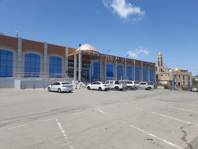 Buildings and shops, asphalt roads paved in mountainous areas during the day, a paved road in the Al-Baha region, street lighting poles, traffic of cars in the streets.