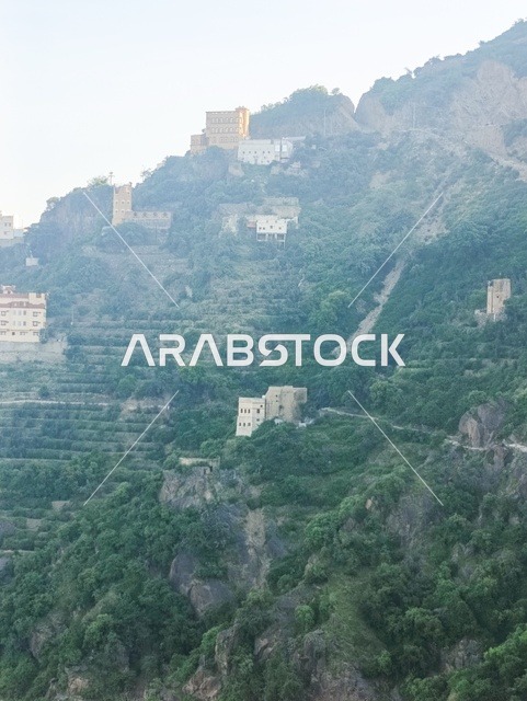 The old traditional houses on the mountains of Faifa in Jazan, southern Saudi Arabia, the peaks and rocky elevations during the day, a natural tourist place and area, the trees and plants and areas of green nature, the agricultural terraces on the mountain slopes.