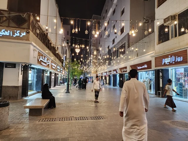 Famous religious landmarks and places at night, urban development and attention to shops and residential buildings, citizens strolling in the illuminated Quba Avenue at night in Medina.