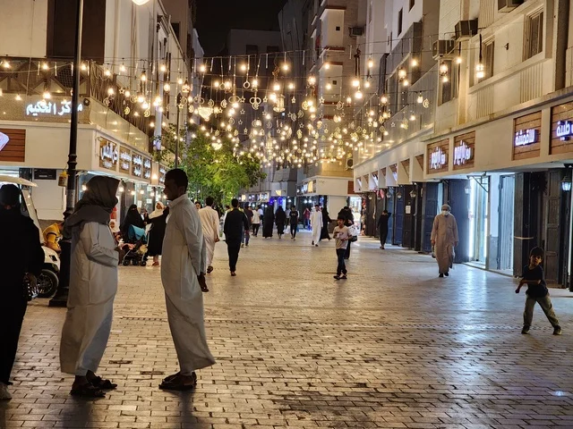 Famous religious landmarks and places at night, urban development and attention to shops and residential buildings, citizens strolling in the illuminated Quba Avenue at night in Medina.