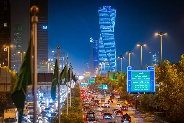 علم المملكة راية التوحيد الخضراء، لوحات طرقية زرقاء، الفن الهندسي المعماري لبرج مضاء في مدينة الرياض في وقت الليل، معالم تجارية واقتصادية وسياحية مشهورة في العاصمة، الفن الهندسي المعماري للمنشآت، النمو والتطور العمراني على الطراز الحديث والمتطور للأبراج