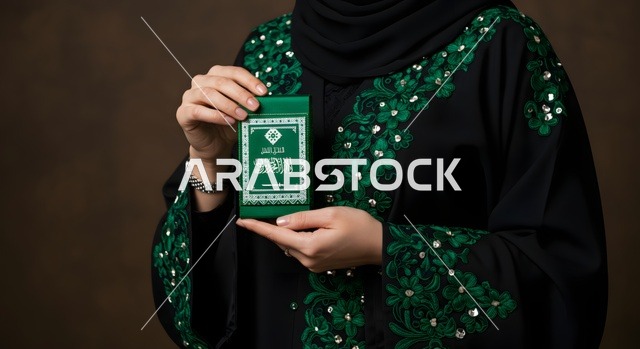 أصالة العادات و التقاليد الخليجية,  امرأة عربية خليجية سعودية محجبة ترتدي العباءة السوداء مع تطريز باللون الاخضر تحمل بيدها كتيب صغير باللون الأخضر مرسوم عليه علم المملكة، خلفية رمادي