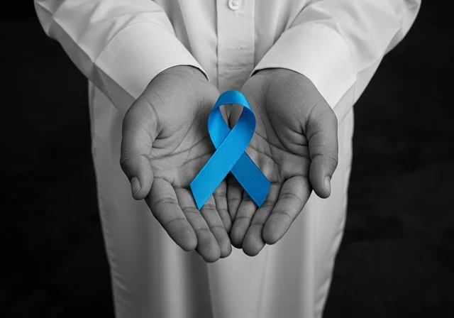 الحفاظ على الصحة الجسدية، شعار الوعي بسرطان البروستاتا ، حملات الإرشاد والتنبيه للكشف المبكر عن سرطان البروستات، بورتريه مقرب لشاب عربي خليجي سعودي يرتدي الزي التقليدي والشماغ يحمل شريط أزرق للتوعية بالأمراض، خلفية سوداء