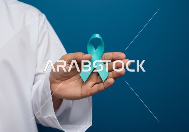 Awareness and alert campaigns for the early detection of prostate cancer, maintaining physical health, the slogan of prostate cancer awareness, a close-up portrait of a young Arab Gulf Saudi man wearing traditional attire and a ghutrah holding a blue ribbon for disease awareness.
