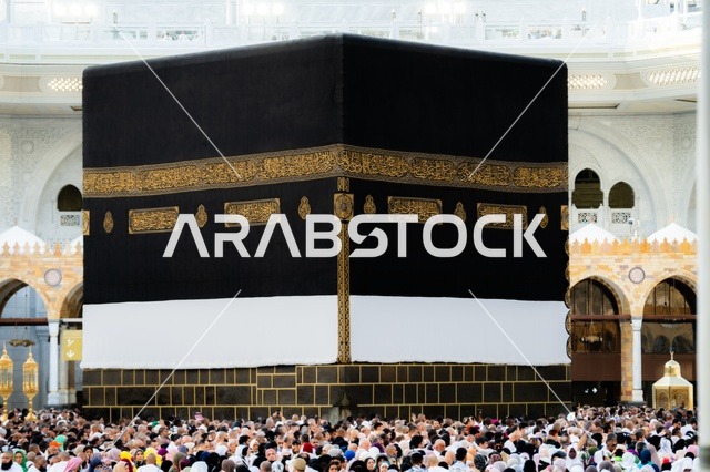 A close-up image of the Holy Kaaba, worship and drawing closer to God, performing the rituals of Hajj and Umrah, the Qibla of Islam and Muslims, the circumambulation of pilgrims and Umrah performers around the Holy Kaaba in Mecca during the day, the minarets surrounding the sanctuary, the House of God in the Sacred Mosque in Mecca, Saudi Arabia.
