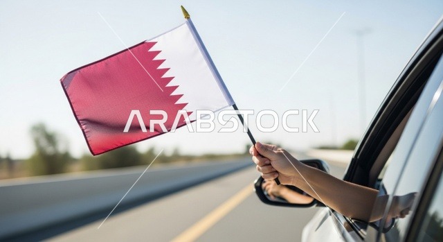 إحياء ذكرى تأسيس الدولة، الاحتفال باليوم الوطني القطري 18 ديسمبر، صورة مقربة ليد رجل عربي خليجي قطري داخل سيارة يحمل علم قطر إلى الخارج بايماءات الفخروالاعتزاز، رموز وثقافات وطنية, حب الوطن والانتماء إليه، تعبير عن الانتماء والهوية القطرية