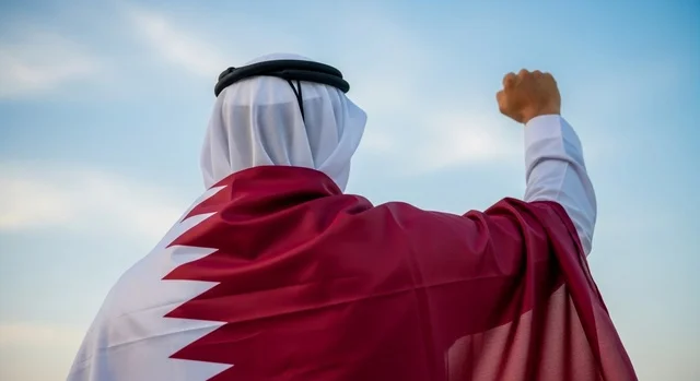 إحياء ذكرى تأسيس الدولة، الاحتفال باليوم الوطني القطري 18 ديسمبر، صورة مقربة لرجل عربي خليجي قطري يقف بثقة وشموخ يضع علم قطرعلى كتفيه بايماءات الفخروالاعتزاز، رموز وثقافات وطنية, حب الوطن والانتماء إليه