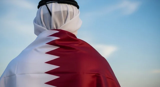 إحياء ذكرى تأسيس الدولة، الاحتفال باليوم الوطني القطري 18 ديسمبر، صورة مقربة لرجل عربي خليجي قطري يقف بثقة وشموخ يضع علم قطرعلى كتفيه بايماءات الفخروالاعتزاز، رموز وثقافات وطنية, حب الوطن والانتماء إليه