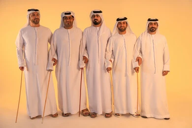 بورتريه لمجموعة من الرجال العرب الخليجيين الإماراتيين يرتدون الكندورة والغترة البيضاء يؤدون رقصة العيالة الشعبية بعصا الخيزران، أجواء تراثية تعبّر عن الفخر بالموروث الثقافي الإماراتي، إيقاعات متناغمة وحركات جماعية تعكس روح الوحدة والاعتزاز بالهوية الوطنية، الحفاظ على التراث الشعبي في المناسبات الوطنية والاجتماعية.