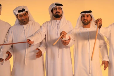 Expressions of pride and appreciation for national identity, a portrait of a group of Emirati Gulf Arab men wearing the kandura and white ghutrah performing the traditional Ayala dance with bamboo sticks, a heritage atmosphere that expresses pride in the Emirati cultural legacy, preserving the folk heritage during national and social occasions.