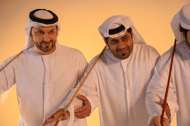 Heritage atmosphere expressing pride in the Emirati cultural heritage, harmonious rhythms and collective movements reflecting the spirit of unity and pride in national identity, a portrait of a group of Emirati Gulf Arab men wearing the kandura and white ghutrah performing the traditional Ayala dance with a bamboo stick, preserving the folk heritage in national and social occasions.