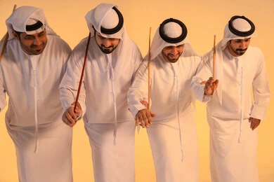 National celebration and belonging, harmonious rhythms and collective movements reflect the spirit of unity and pride in national identity. A group of Emirati Gulf Arab men wearing the kandura and white ghutrah perform the traditional Ayala dance with bamboo sticks. The atmosphere is cultural, expressing pride in the Emirati cultural heritage and preserving the folk heritage during national and social occasions.