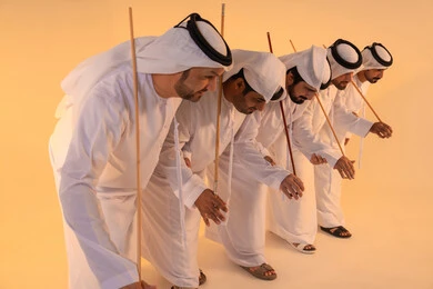Pride in Emirati customs and traditions, harmonious rhythms and collective movements reflect the spirit of unity and pride in national identity. A group of Emirati Gulf Arab men wearing the kandura and white ghutrah perform the traditional Ayala dance with bamboo sticks, preserving the folk heritage during national and social occasions.