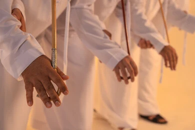 Preserving the folk heritage during national and social occasions, harmonious rhythms and collective movements reflect the spirit of unity and pride in national identity. A group of Emirati Gulf Arab men wearing the kandura and white ghutrah perform the traditional Ayala dance with bamboo sticks, creating a heritage atmosphere that expresses pride in the Emirati cultural legacy, preserving the folk heritage during national and social occasions.