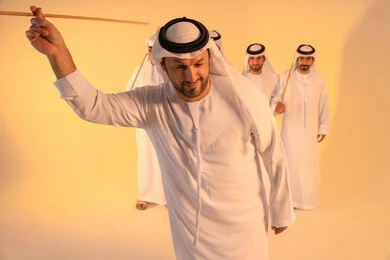 Celebration and national belonging, embodying pride in Emirati customs and traditions, an Arab Gulf Emirati man wearing the kandura and ghutrah performing the Ayala dance with a bamboo stick, a joyful festive atmosphere, preserving the popular heritage and cultural identity during national and social occasions.