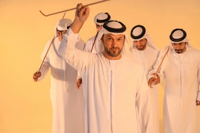 Preserving cultural heritage and authentic traditions, celebrating national and heritage occasions, performing Emirati folk arts, a close portrait of a group of Emirati Gulf Arab men wearing the kandura and ghutrah performing the traditional Ayala dance, gestures of joy and pride in national identity.