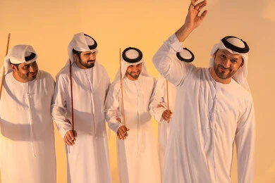 Preserving the folk heritage during national and social occasions, harmonious rhythms and collective movements reflect the spirit of unity and pride in national identity. A group of Emirati Gulf Arab men wearing the kandura and white ghutrah perform the traditional Ayala dance with bamboo sticks, creating a heritage atmosphere that expresses pride in the Emirati cultural legacy, preserving the folk heritage during national and social occasions.
