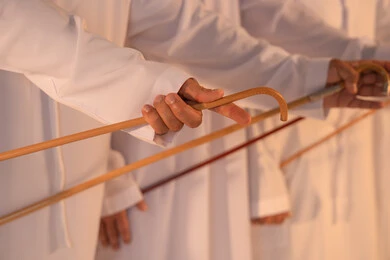Pride in Emirati customs and traditions, harmonious rhythms and collective movements reflect the spirit of unity and pride in national identity. A group of Emirati Gulf Arab men wearing the kandura and white ghutrah perform the traditional Ayala dance with bamboo sticks, preserving the folk heritage during national and social occasions.