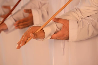 National celebration and belonging, harmonious rhythms and collective movements reflect the spirit of unity and pride in national identity. A group of Emirati Gulf Arab men wearing the kandura and white ghutrah perform the traditional Ayala dance with bamboo sticks. The atmosphere is cultural, expressing pride in the Emirati cultural heritage and preserving the folk heritage during national and social occasions.