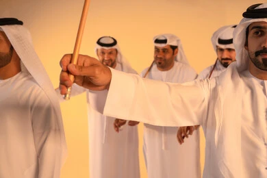 Celebration and national belonging, embodying pride in Emirati customs and traditions, a close-up portrait of the hand of an Emirati Gulf Arab man wearing the kandura and ghutrah performing the Ayala dance with a bamboo stick, a joyful festive atmosphere, preserving the popular heritage and cultural identity during national and social occasions.