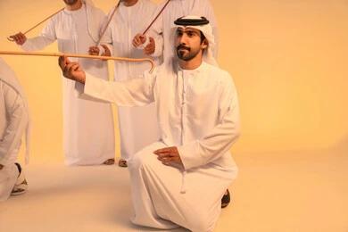 Celebration and national belonging, embodying pride in Emirati customs and traditions, an Arab Gulf Emirati man wearing the kandura and ghutrah performing the Ayala dance with a bamboo stick, a joyful festive atmosphere, preserving the popular heritage and cultural identity during national and social occasions.