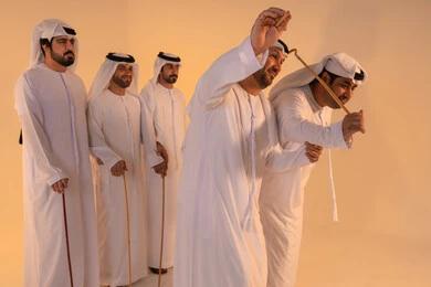 تعابير الفخر والاعتزاز، مظاهر الفرح والاحتفاء بالتراث الإماراتي الأصيل، بورتريه لمجموعة من الرجال العرب الخليجيين الإماراتيين يرتدون الكندورة والغترة يؤدون رقصة العيالة التقليدية بالعصي الخشبية، تجسيد للهوية الوطنية والانتماء، الحفاظ على العادات والتقاليد الشعبية في المناسبات الوطنية، أجواء احتفالية مفعمة بالفخر والاعتزاز.