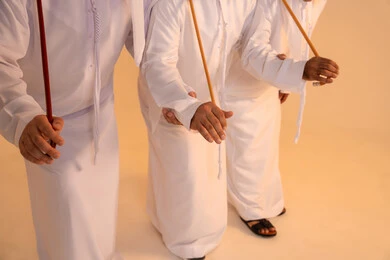 مظاهر الأصالة والعزة في المناسبات الوطنية، الاحتفال بالمناسبات الوطنية والتراثية، أداء الفنون الشعبية الإماراتية، بورترية مقرب ليد مجموعة من الرجال العرب الخليجيين الإماراتيين يرتدون الكندورة والغترة يقومون بعرض رقصة العيالة التراثية، إيماءات السرور والفخر بالهوية الوطنية، الحفاظ على الموروث الثقافي والعادات الأصيلة