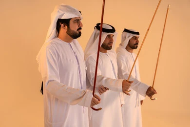 Celebrating national and heritage occasions, performing Emirati folk arts, a portrait of a group of Arab Gulf Emirati men wearing the kandura and ghutrah performing the traditional Ayala dance, gestures of joy and pride in national identity, preserving cultural heritage and authentic customs.
