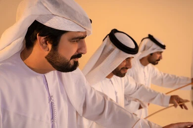 أجواء احتفالية مفعمة بالفخر والاعتزاز، مظاهر الفرح والاحتفاء بالتراث الإماراتي الأصيل، بورتريه لمجموعة من الرجال العرب الخليجيين الإماراتيين يرتدون الكندورة والغترة يؤدون رقصة العيالة التقليدية بالعصي الخشبية، تجسيد للهوية الوطنية والانتماء، الحفاظ على العادات والتقاليد الشعبية في المناسبات الوطنية