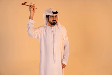 مشاركة في الفعاليات التراثية والمناسبات الوطنية،الاحتفال بالموروث الشعبي الإماراتي، بورتريه لرجل عربي خليجي إماراتي يرتدي الكندورة والغترة يؤدي رقصة العيالة بالعصا الخشبية، إيماءات فخر واعتزاز بالهوية الوطنية، الحفاظ على التراث الثقافي الأصيل.