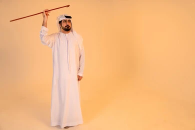 الحفاظ على التراث الثقافي الأصيل، الاحتفال بالموروث الشعبي الإماراتي، بورتريه لرجل عربي خليجي إماراتي يرتدي الكندورة والغترة يؤدي رقصة العيالة بالعصا الخشبية، إيماءات فخر واعتزاز بالهوية الوطنية، مشاركة في الفعاليات التراثية والمناسبات الوطنية