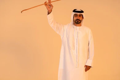 إيماءات فخر واعتزاز بالهوية الوطنية، مشاركة في الفعاليات التراثية والمناسبات الوطنية، الاحتفال بالموروث الشعبي الإماراتي، بورتريه لرجل عربي خليجي إماراتي يرتدي الكندورة والغترة يؤدي رقصة العيالة بالعصا الخشبية، الحفاظ على التراث الثقافي الأصيل.