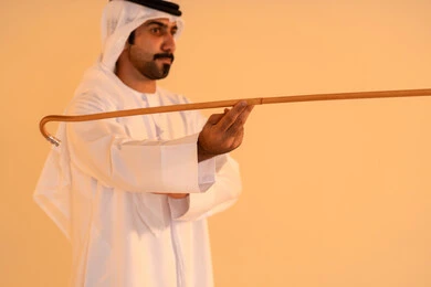 الاحتفال بالموروث الشعبي الإماراتي، بورتريه لرجل عربي خليجي إماراتي يرتدي الكندورة والغترة يؤدي رقصة العيالة بالعصا الخشبية، إيماءات فخر واعتزاز بالهوية الوطنية، مشاركة في الفعاليات التراثية والمناسبات الوطنية، الحفاظ على التراث الثقافي الأصيل.