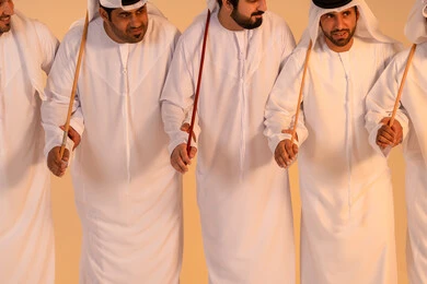 A portrait of a group of Emirati Gulf Arab men wearing the kandura and ghutrah performing the traditional Ayala dance, gestures of joy and pride in national identity, celebrating national and heritage occasions, performing Emirati folk arts, preserving cultural heritage and authentic traditions.