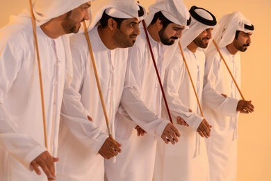 Expressions of joy and celebration of the authentic Emirati heritage, a portrait of a group of Emirati Gulf Arab men wearing the kandura and ghutrah performing the traditional Ayala dance with wooden sticks, embodying national identity and belonging, preserving customs and traditions during national occasions, a festive atmosphere filled with pride and honor.
