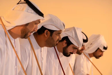 أداء الفنون الشعبية الإماراتية، الاحتفال بالمناسبات الوطنية والتراثية، بورترية لمجموعة من الرجال العرب الخليجيين الإماراتيين يرتدون الكندورة والغترة  يقومون بعرض رقصة العيالة التراثية، إيماءات السرور والفخر بالهوية الوطنية، الحفاظ على الموروث الثقافي والعادات الأصيلة
