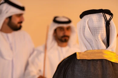 Gestures of pride and honor, manifestations of joy and celebration of the authentic Emirati heritage, a portrait of a group of Arab Gulf Emirati men wearing the kandura and ghutrah performing the traditional Ayala dance with wooden sticks, embodying national identity and belonging, preserving popular customs and traditions during national occasions.