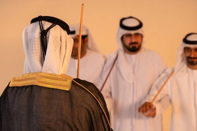 Expressions of joy and celebration, a portrait of a group of Emirati Gulf Arab men wearing the kandura and ghutrah performing the traditional Ayala dance with wooden sticks, embodying national identity and belonging, preserving popular customs and traditions during national occasions, a festive atmosphere filled with pride and honor.
