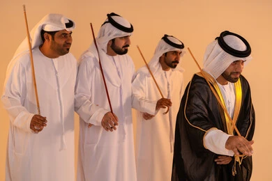 أجواء احتفالية مفعمة بالفخر والاعتزاز، مظاهر الفرح والاحتفاء بالتراث الإماراتي الأصيل، بورتريه لمجموعة من الرجال العرب الخليجيين الإماراتيين يرتدون الكندورة والغترة يؤدون رقصة العيالة التقليدية بالعصي الخشبية، تجسيد للهوية الوطنية والانتماء، الحفاظ على العادات والتقاليد الشعبية في المناسبات الوطنية