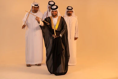 Preserving popular customs and traditions during national occasions, expressions of joy and celebration of the authentic Emirati heritage, a portrait of a group of Emirati Gulf Arab men wearing the kandura and ghutrah performing the traditional Ayala dance with wooden sticks, embodying national identity and belonging, a festive atmosphere filled with pride and honor.