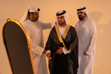 مفهوم الأناقة والفخامه، الاعتزاز بالهوية والتراث الإماراتي الأصيل ، بورتريه لرجل عربي خليجي إماراتي يرتدي البشت الأسود المطرز بالذهبي بمساعدة صديقين، الاستعداد للمناسبات الرسمية والاحتفالات الوطنية
