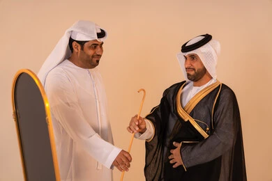 Brotherhood and cooperation in preparing for official occasions, manifestations of authenticity and grandeur, a portrait of an Emirati Gulf Arab man wearing a black bisht embroidered with gold with the help of his friend, the concept of elegance and attention to appearance, preparation for national celebrations.