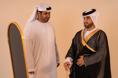الاعتزاز بالهوية الاماراتية ، الأخوة والتعاون في التحضير للمناسبات الرسمية، مظاهر الأصالة والفخامة، بورتريه لرجل عربي خليجي إماراتي يرتدي البشت الأسود المطرز بالذهبي بمساعدة صديقه، مفهوم الاناقة والاهتمام بالمظهر الخارجي ، الاستعداد للاحتفالات الوطنية