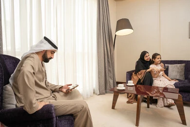 تصفح وسائل التواصل الاجتماعي باستخدام االجوال، اجواء عائلية سعيدة، تعابير الفرح والسرور، برنامج كوميدي ترفيهي، قضاء وقت الفراغ بالتسلية والترفيه,عائلة عربيه خليجيه اماراتية ترتدي الزي التقليدي تجلس فى غرفه المعيشة يقومون بمشاهدة الفلم والمسلسل
