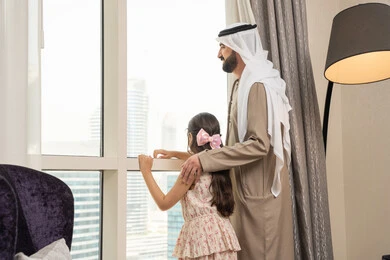 قضاء أوقات عائلية ممتعة، مفهوم الهمة والنشاط، رجل عربي خليجي اماراتي يقف امام النافذة برفقة ابنته، النظر الى الخارج ، إشراقة يوم جديد، الاستمتاع بمشاهده المناظر الطبيعية