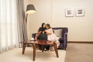 دمج التعلم بالتقنية والتكنولوجيا، مشاهدة الأنشطة الترفيهية والتعليمية، اهتمام الآباء بالأبناء، متابعة منصات التعليم الالكتروني عبر الانترنت، امراه عربية خليجية سعودية ترتدي الحجاب والعباءة تجلس على الاريكة برفقة ابنتها تستخدم جهاز التابلت