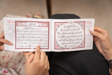 تقوية الفطرة الدينية عند الأطفال، الإجتهاد و الخشوع في العباده، تلاوة وقراءة كتاب الله تعالى، صورة مقربة ليد ام عربيه خليجيه سعودية تقوم بقراءة القراة الكريم برفقة ابنتها