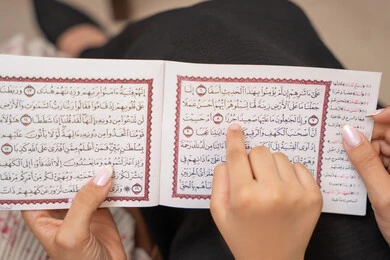 تلاوة وقراءة كتاب الله تعالى، صورة مقربة ليد ام عربيه خليجيه سعودية تقوم بقراءة القراة الكريم برفقة ابنتها، الإجتهاد و الخشوع في العباده، تعزيز الفطرة الاسلامية لدى الاولاد